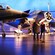 A guide talking to 2 Guests at an exhibit of 2 planes and a helicopter at the Air Force Museum of New Zealand